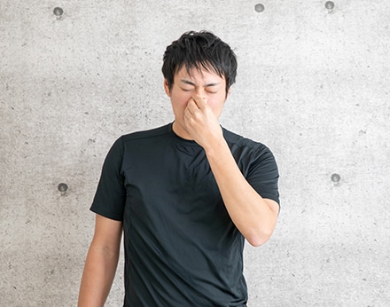 鼻の付け根を押さえ不調を感じる男性、アレルギー症状を表現